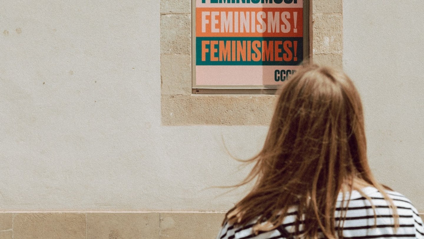 Una mujer ante un cartel en el que pone "feminismos"