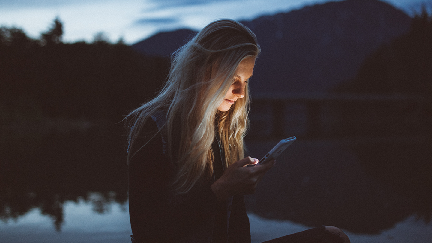una chica rubia mira su móvil en un lago por la noche