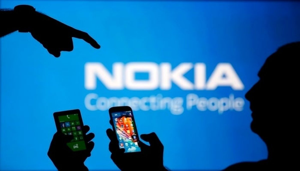 Men are silhouetted against a video screen with an Nokia logo as he poses with an Nokia Lumia 820 and Samsung S4 smartphones in this photo illustration taken in the central Bosnian town of Zenica
